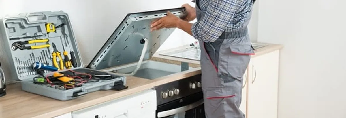 Cooktop repair technician lifting a built-in stovetop for service in Kansas City, KS