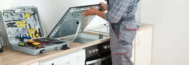 Cooktop repair technician lifting a built-in stovetop for service in Kansas City, KS