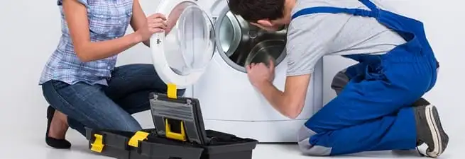Washer repair technician inspecting a front-load washing machine with tools in Kansas City, KS