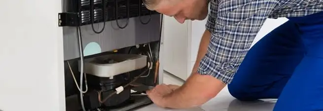 Refrigerator repair technician servicing the compressor and condenser area in Kansas City, KS