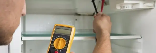 Refrigerator repair technician testing electrical components with a multimeter in Kansas City, KS