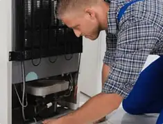 Refrigerator repair technician servicing the compressor and condenser area in Kansas City, KS