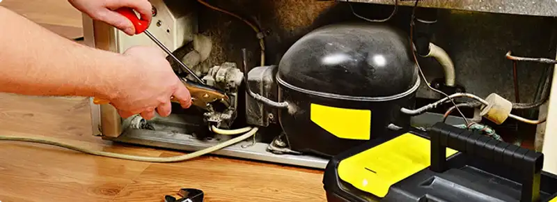 Refrigerator repair technician fixing the compressor and wiring in Kansas City, KS